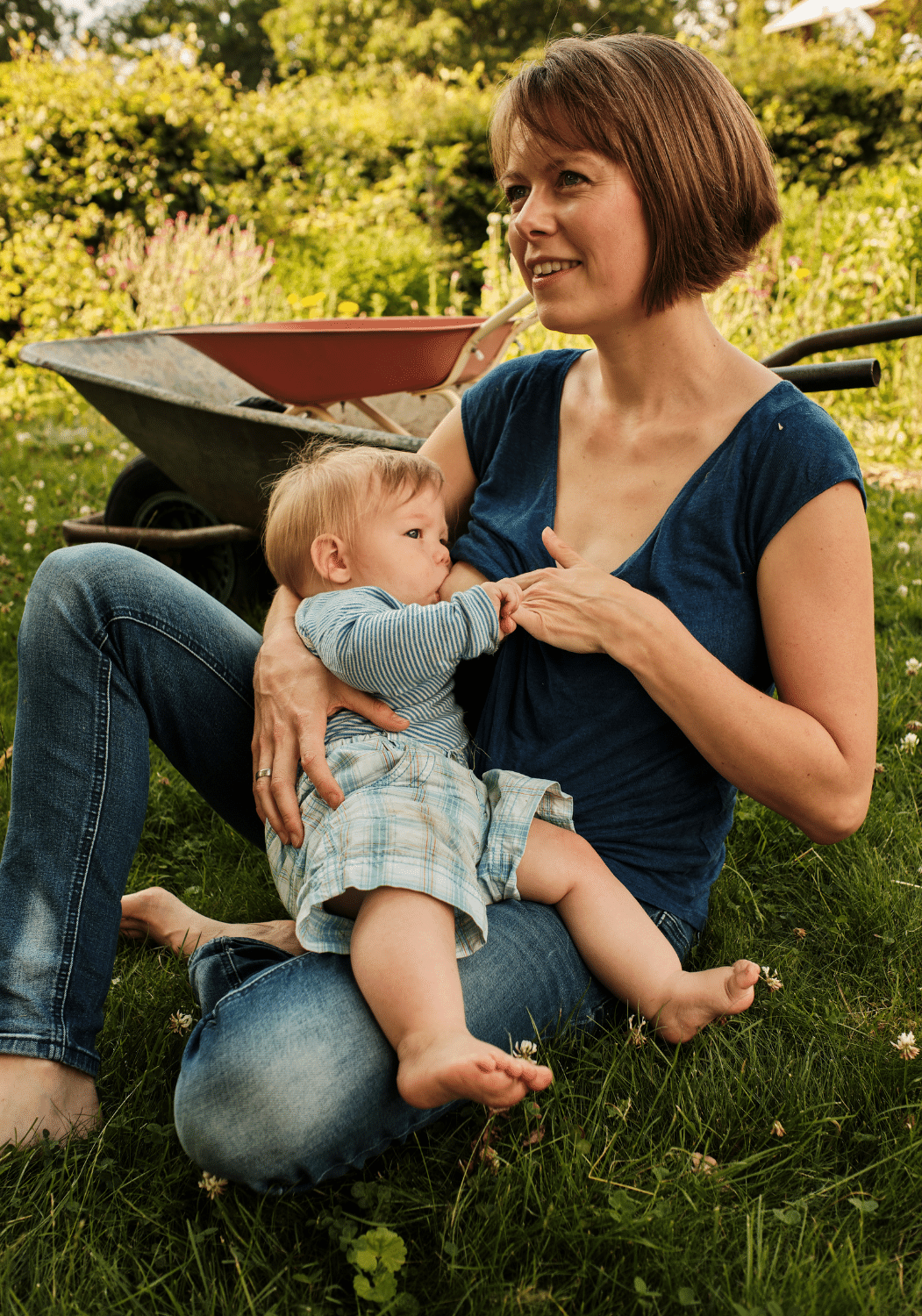 Frau sitzt im Garten vor einer Schubkarre und stillt ihr Kleinkind